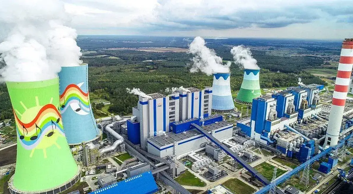 Kolorowe kominy chłodni w elektrowni Dolna Odra, z tęczami i nutami, na tle przemysłowego kompleksu i zielonego krajobrazu.